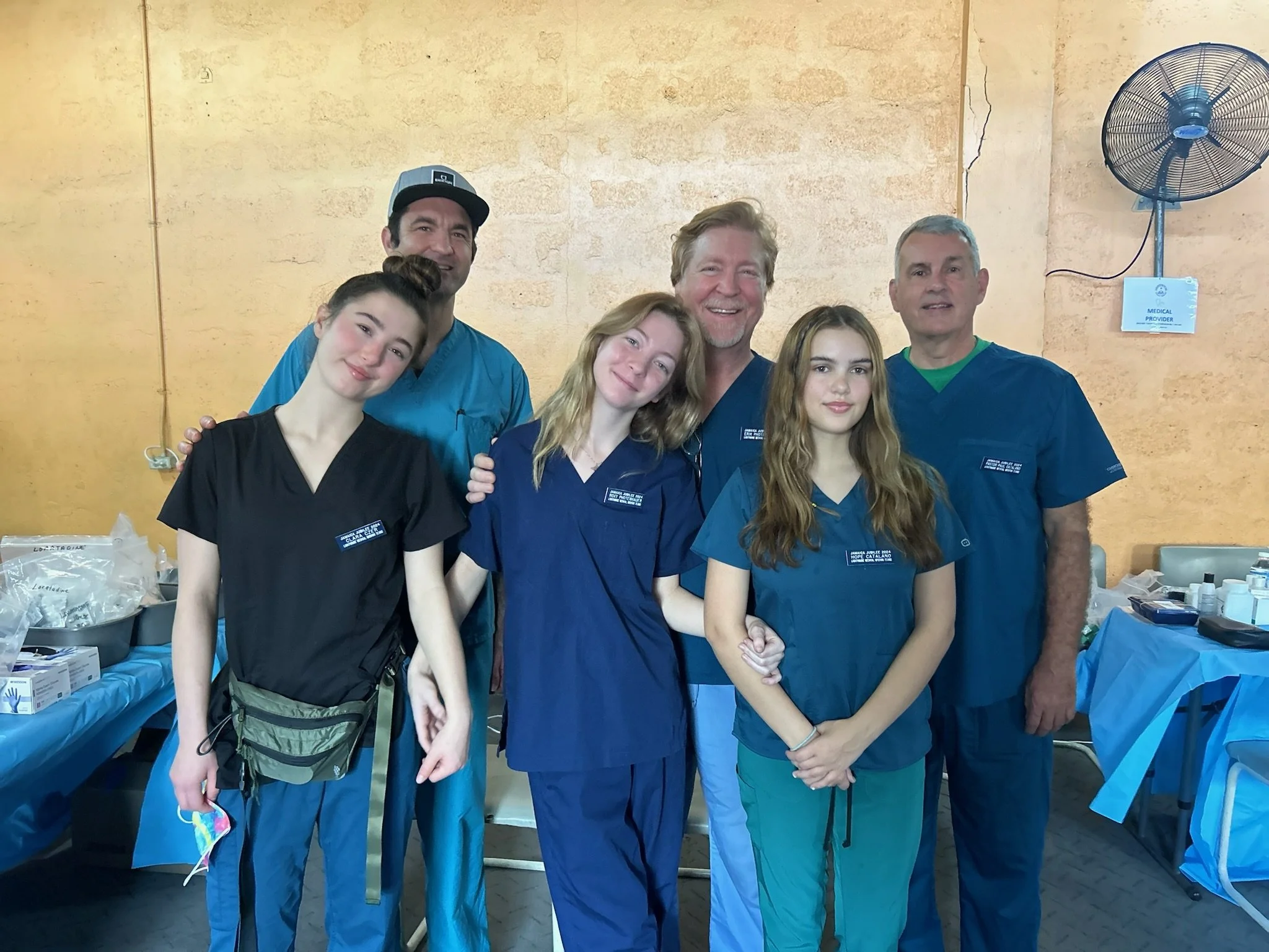 Group of six healthcare professionals, four women and two men, standing together in a medical setting, smiling at the camera.