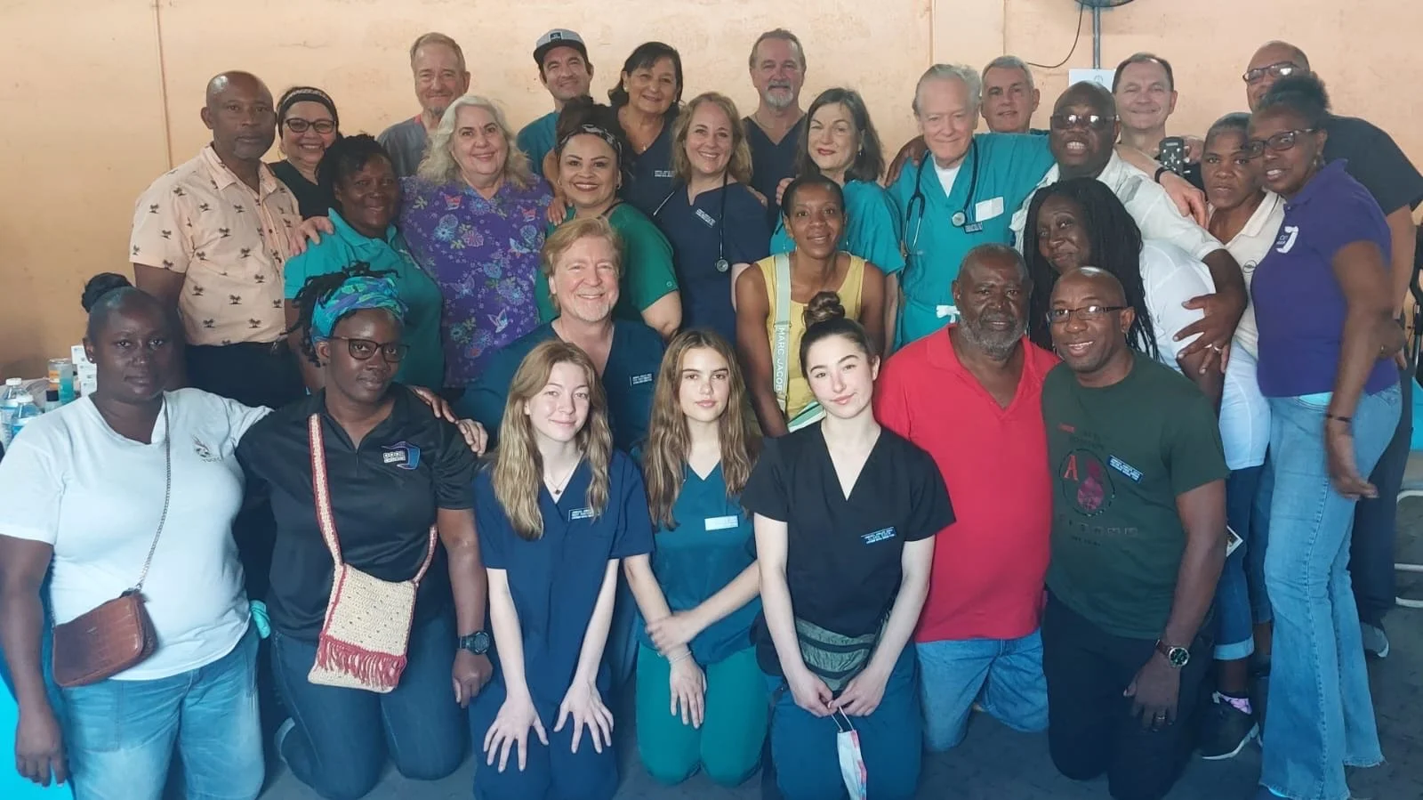 Group of diverse healthcare professionals and volunteers posing together in a room, smiling at the camera.