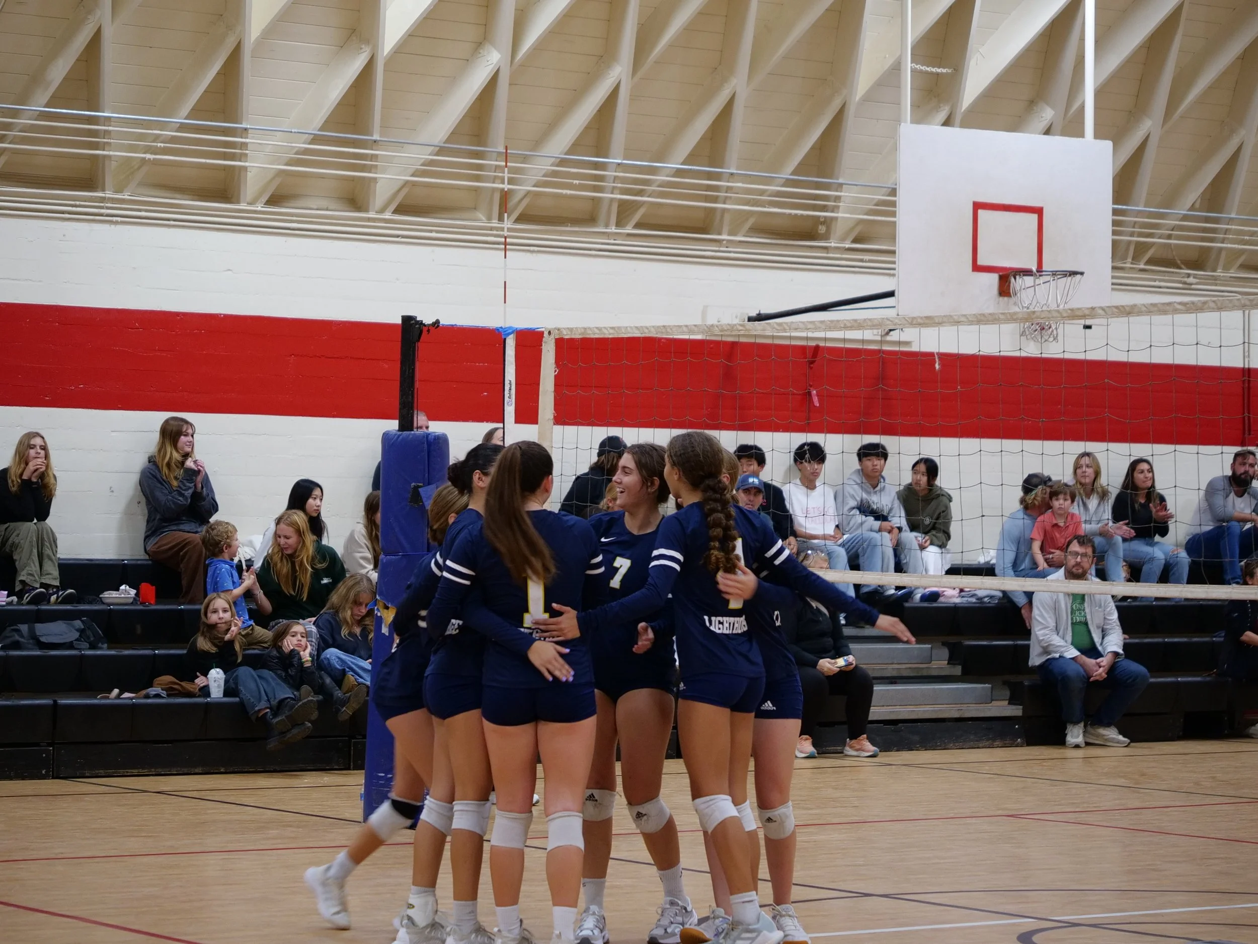 Indoor volleyball game with players celebrating and spectators watching.