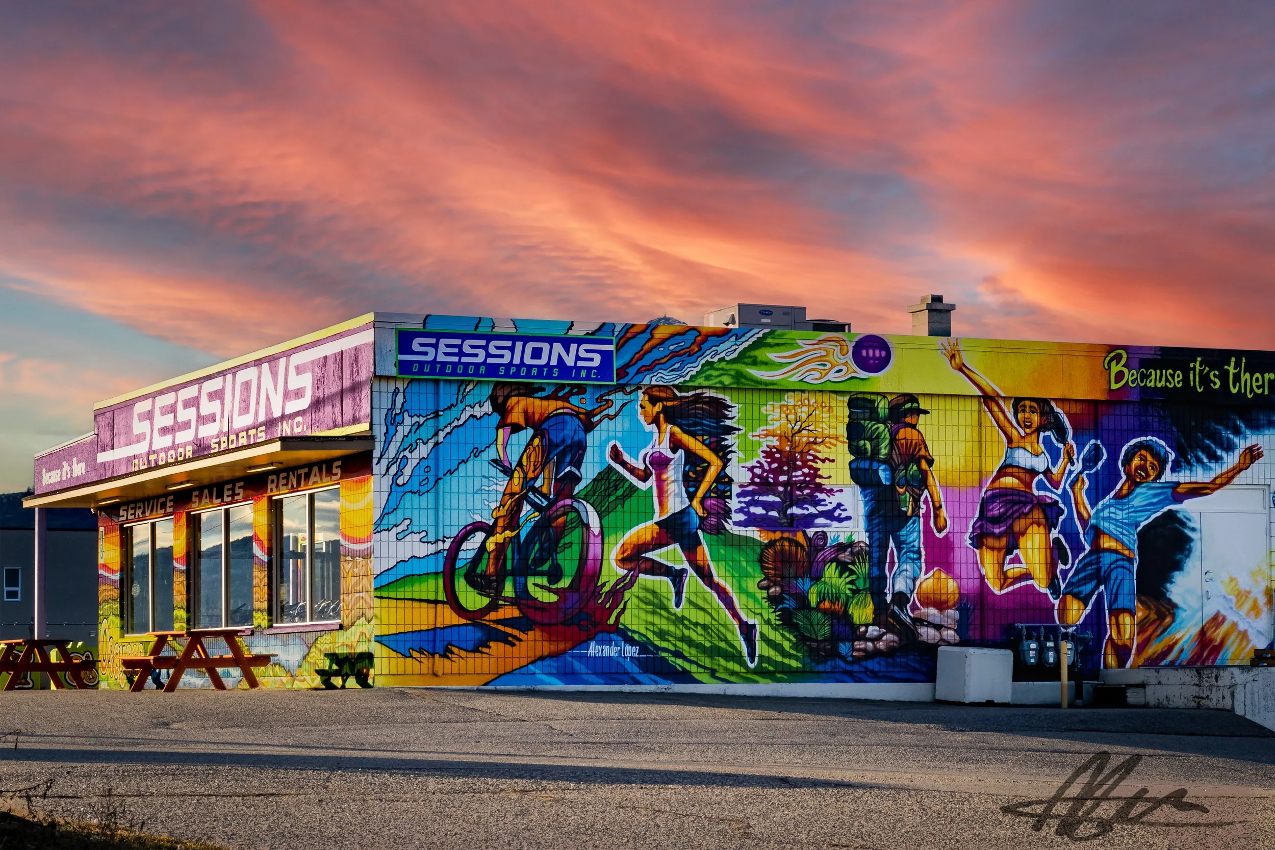 Colorful mural on a building wall depicting outdoor sports scenes including cycling, running, hiking, and jumping, with a sunset sky in the background.