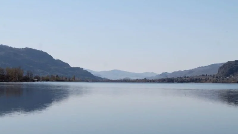 A calm river or lake surrounded by mountains and hills under a clear blue sky.