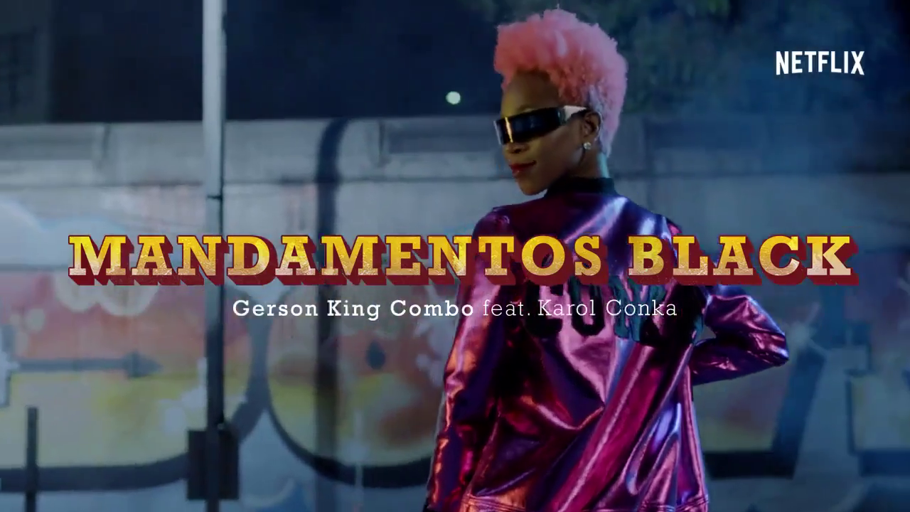 A woman with pink hair wearing futuristic sunglasses and a shiny purple jacket, standing outdoors with graffiti art in the background. The image features the title 'MANDAMENTOS BLACK' and the text 'Gerson King Combo feat. Karol Conka' for a Netflix r