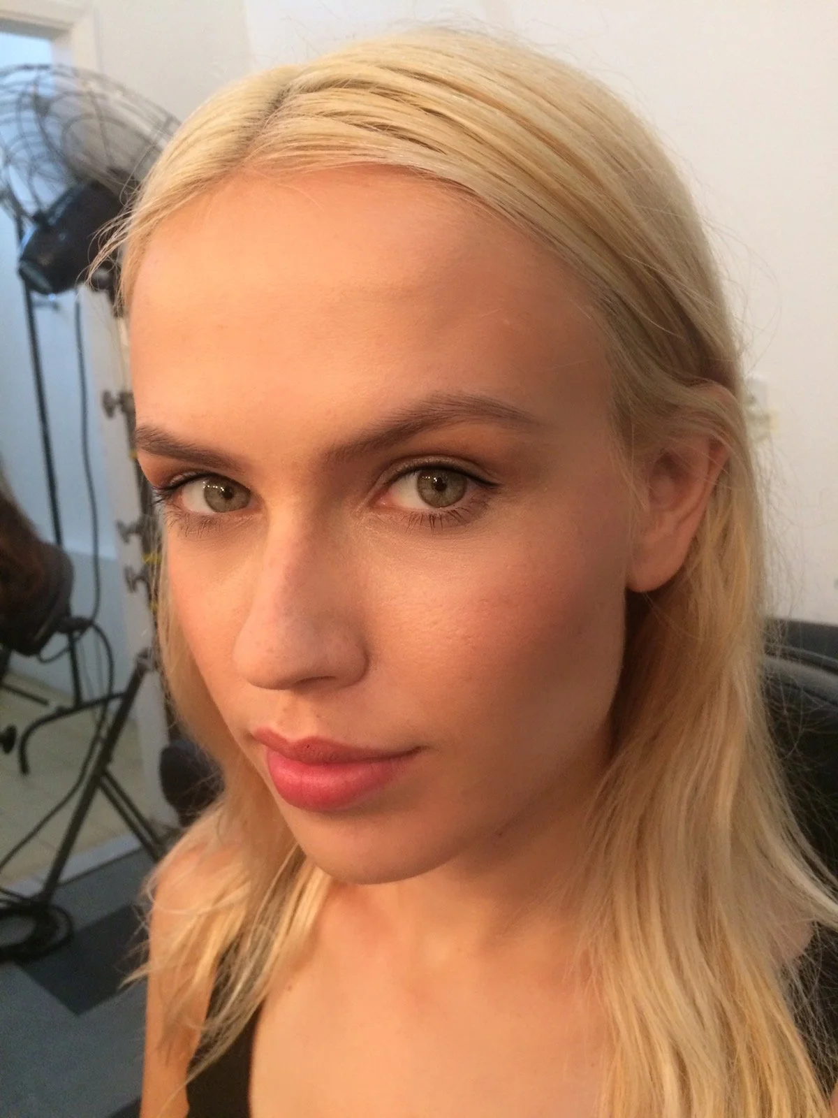 Close-up of a woman with blonde hair, light skin, and makeup, in a photography studio setting.