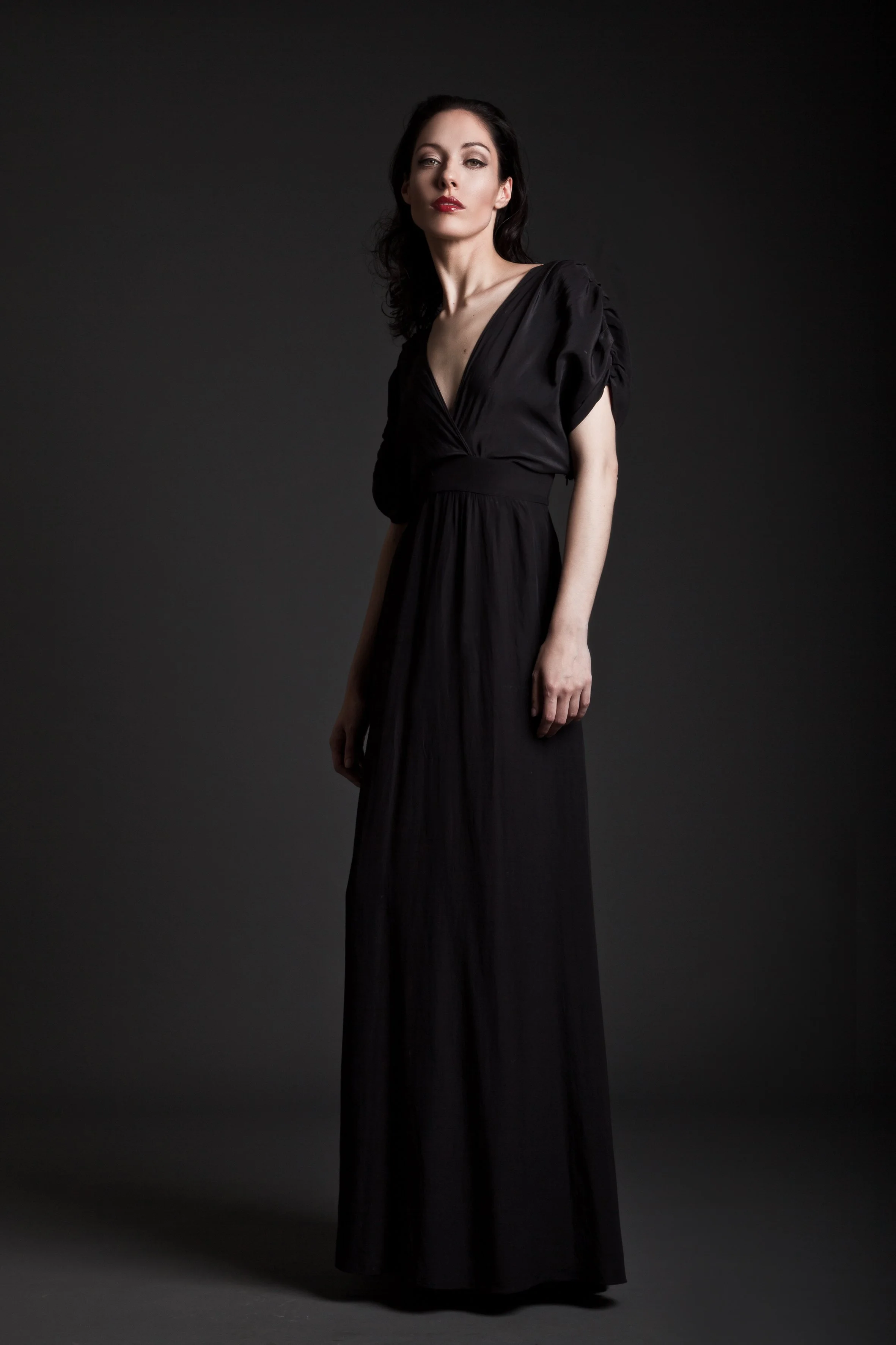 A woman in a long black dress standing against a dark background.