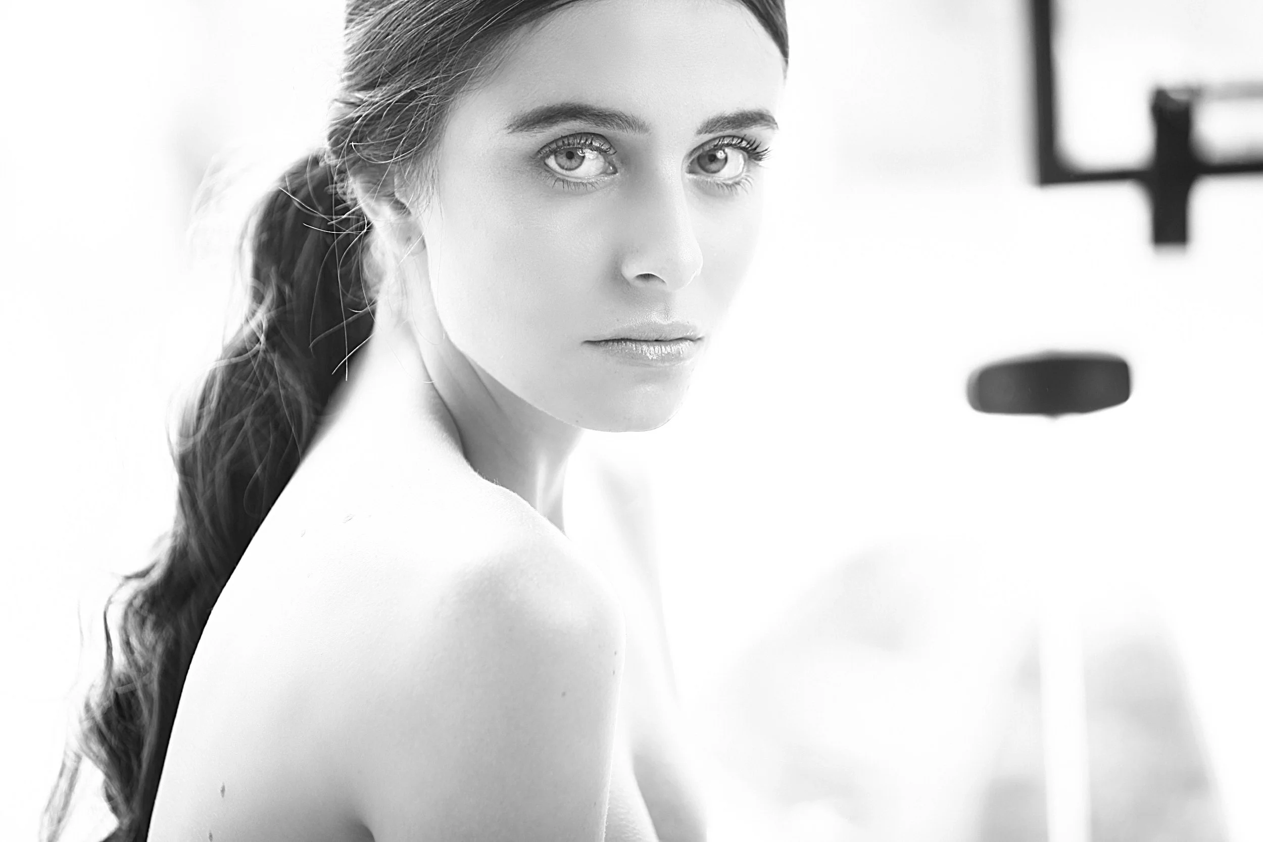 A black-and-white photo of a woman with long hair, looking directly at the camera, with a blurred background.
