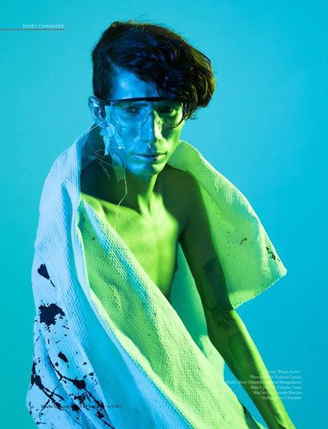 A woman with short black hair, wearing translucent glasses, draped in a towel, against a blue background with green lighting effects.
