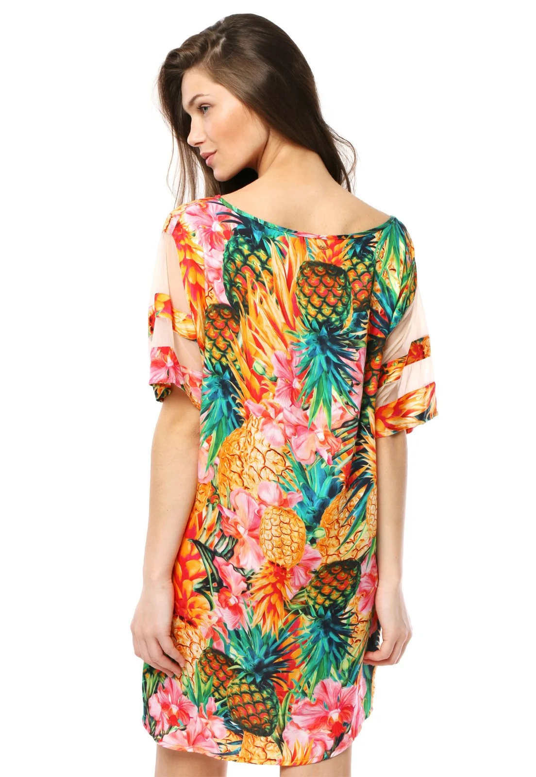 Woman wearing a colorful tropical print dress with pineapples, pineapples, and flowers, viewed from the back.
