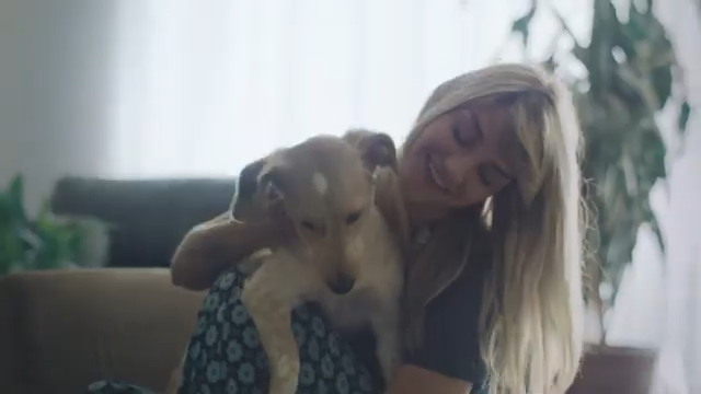 A woman embracing a small dog inside a home with natural light and houseplants.