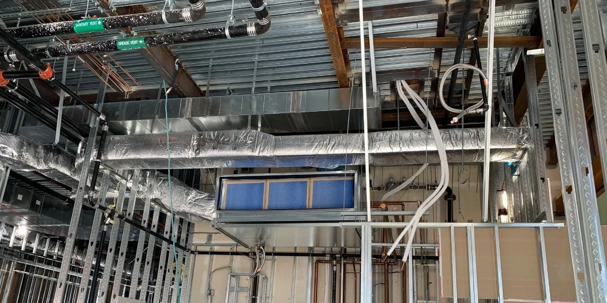 Construction site with metal framing, HVAC ducts, pipes, and electrical wiring