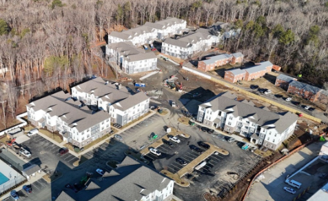 An aerial view of a residential apartment complex with multiple buildings, parking lots, and surrounding trees.