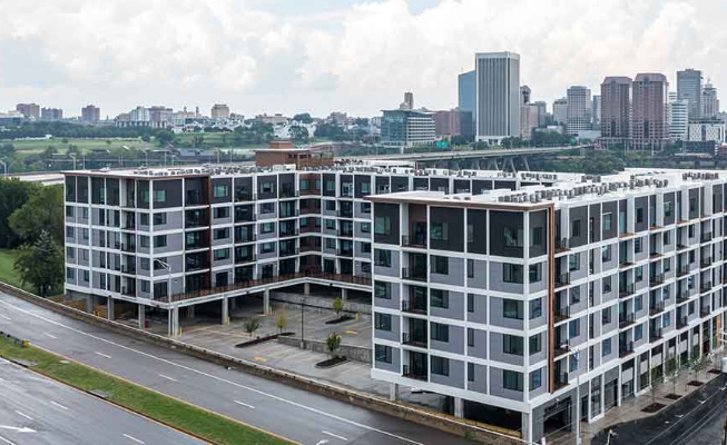 Modern multi-story residential buildings in the foreground with a city skyline in the background, featuring tall office buildings and skyscrapers.