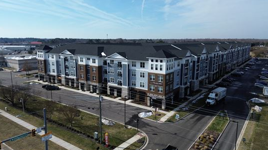 A large multi-story apartment complex with retail stores on the ground level, surrounded by parking lots and streets.