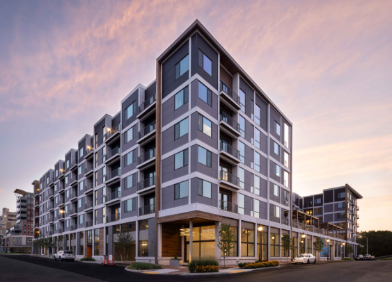 Modern multi-story apartment building at sunset with street view and parked cars.