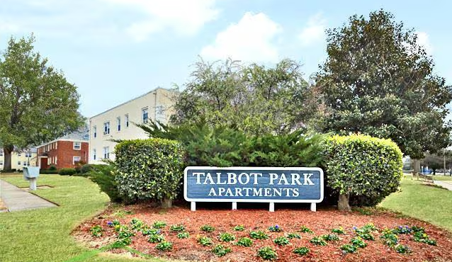Sign for Talbot Park Apartments with landscaped bushes and flowers in front, and apartment buildings in the background.