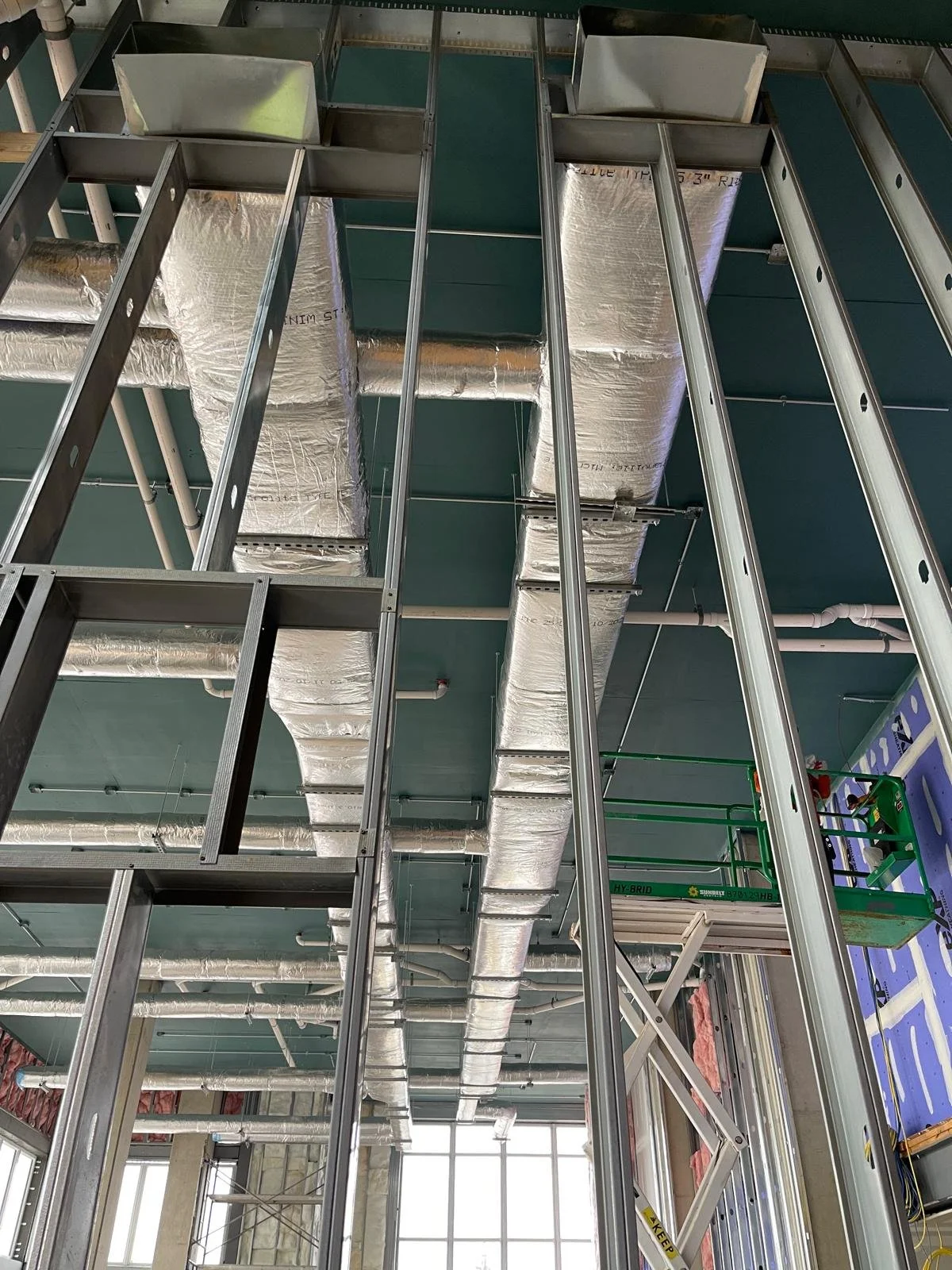 Construction site with metal framing, ductwork, and scaffolding inside a building under construction.