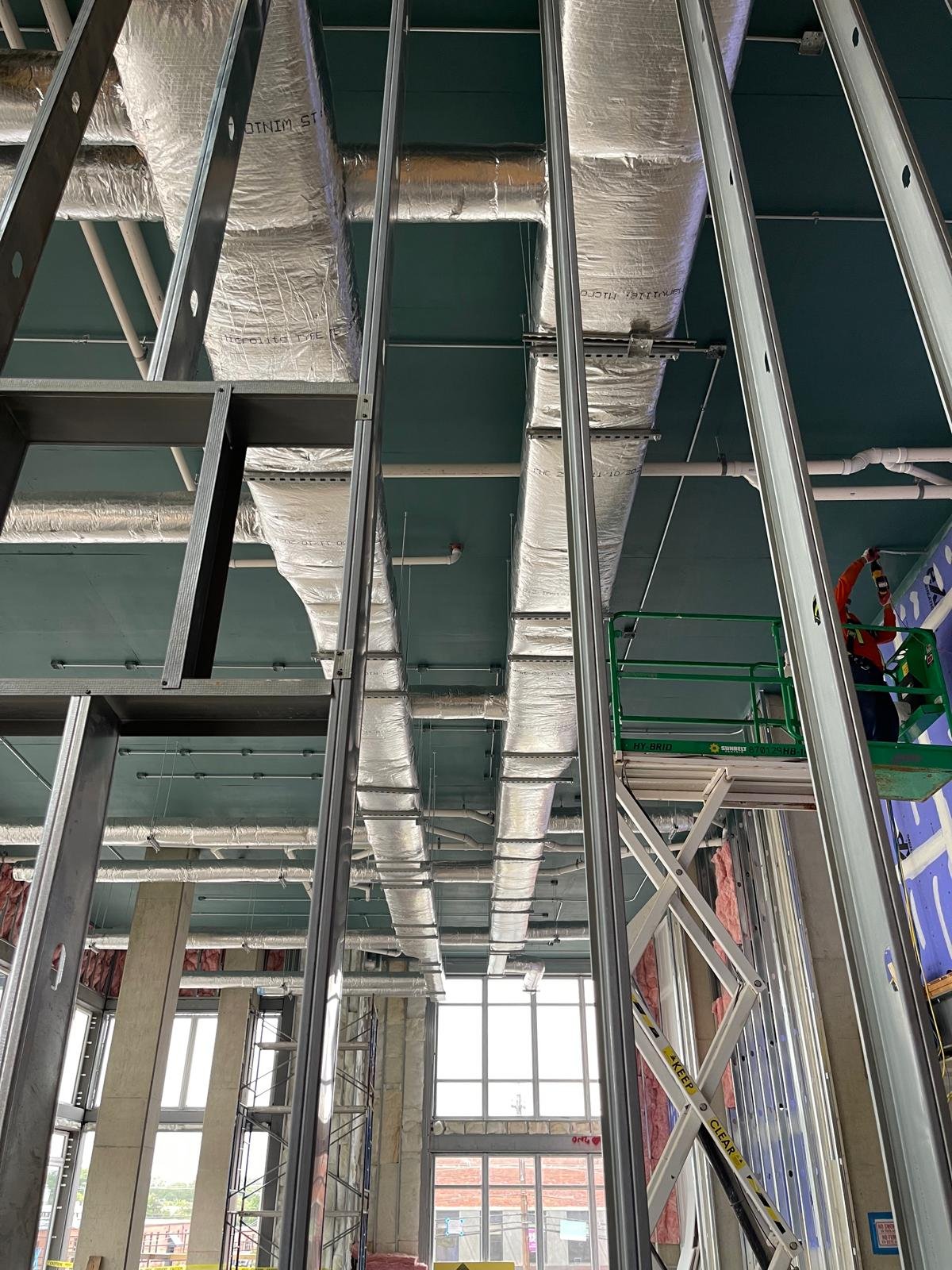 Construction site with metal framing, ductwork, and scaffolding, in a partially built interior space.