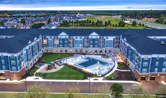 Aerial view of a modern residential complex with a central courtyard featuring a swimming pool, playground, and landscaped gardens, surrounded by multiple apartment buildings.
