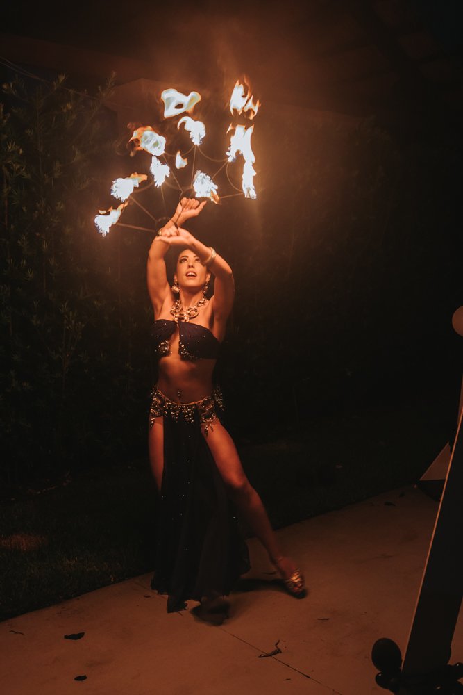 A woman performing a fire dance at night, holding fire poi, with flames creating circles above her head.