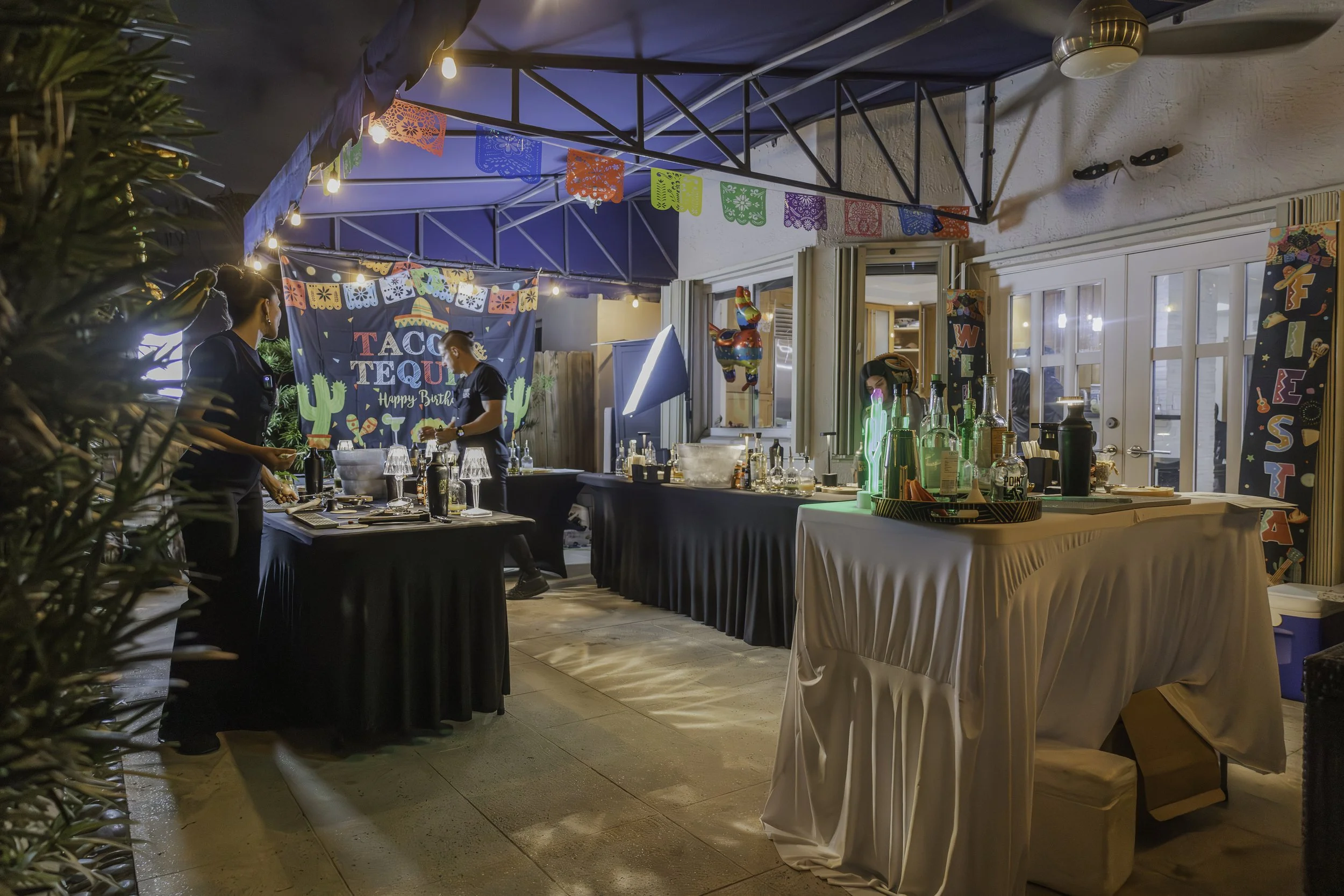Decorated outdoor patio for a birthday celebration with colorful papel picado banners, a 'Taco Tequila' birthday sign, and tables set for drinks and food.