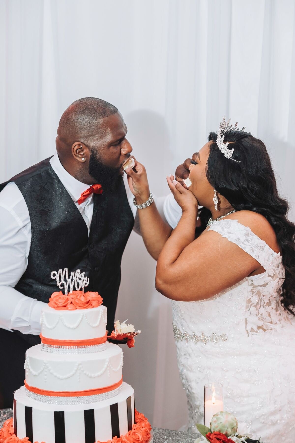 A bride and groom sharing cake at their wedding reception, with a tiered wedding cake decorated with orange roses, black and white stripes, and 'Mr & Mrs' topper.