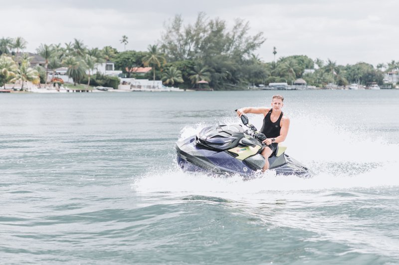 Person riding a jet ski on a lake with houses and trees in the background.
