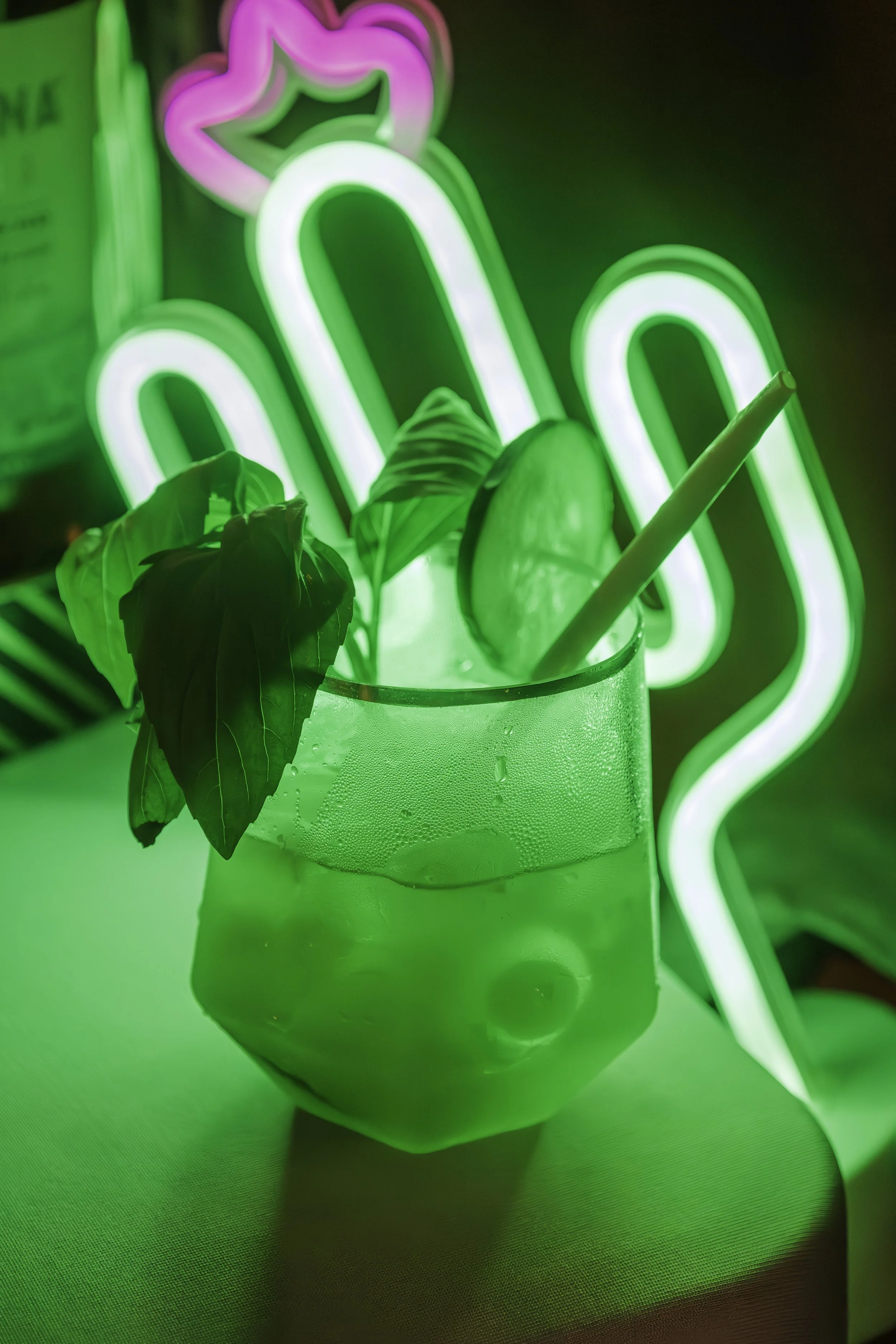 Neon green and pink neon sign behind a plant in a glass of water, with a green neon light illuminating the scene.