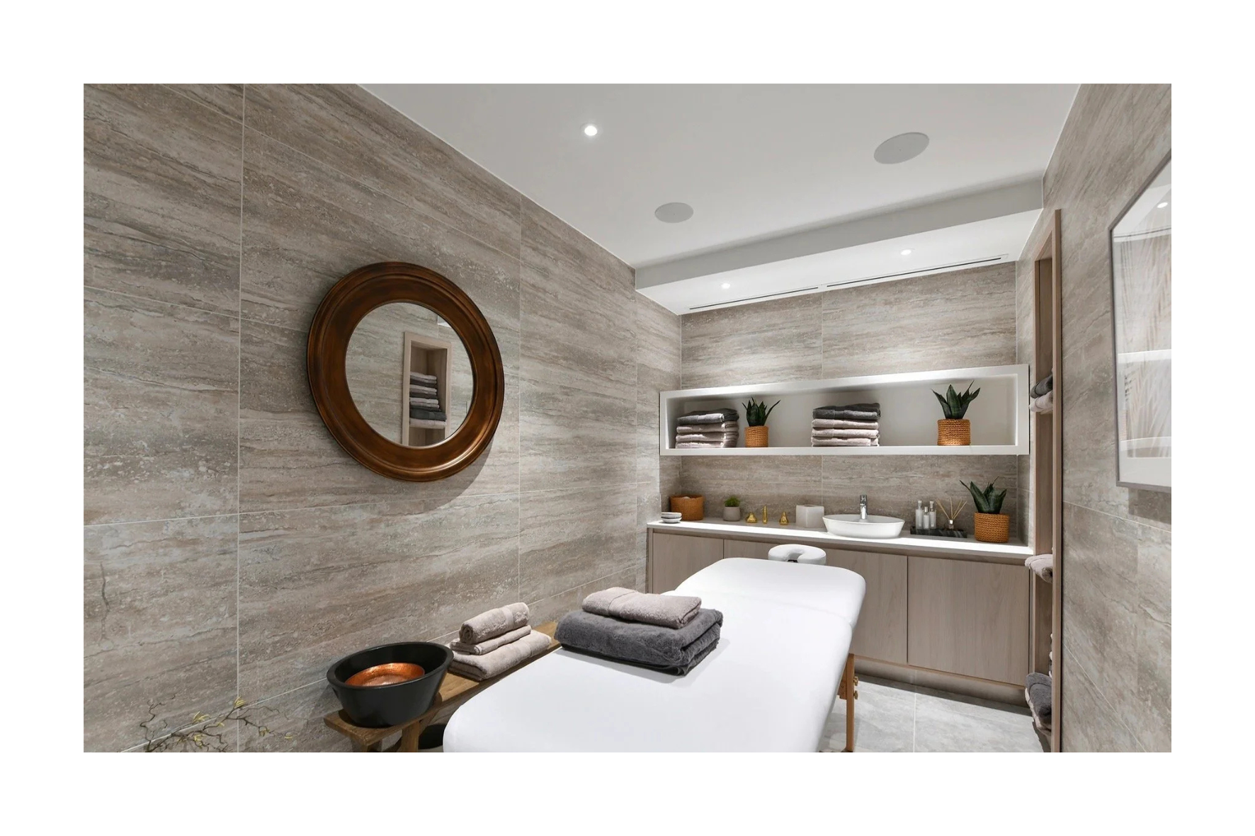 Modern bathroom with beige textured tile walls, white ceiling with recessed lighting, and a white bathtub with towels on a wooden stool. The shelves hold rolled towels, potted plants, and decorative items.