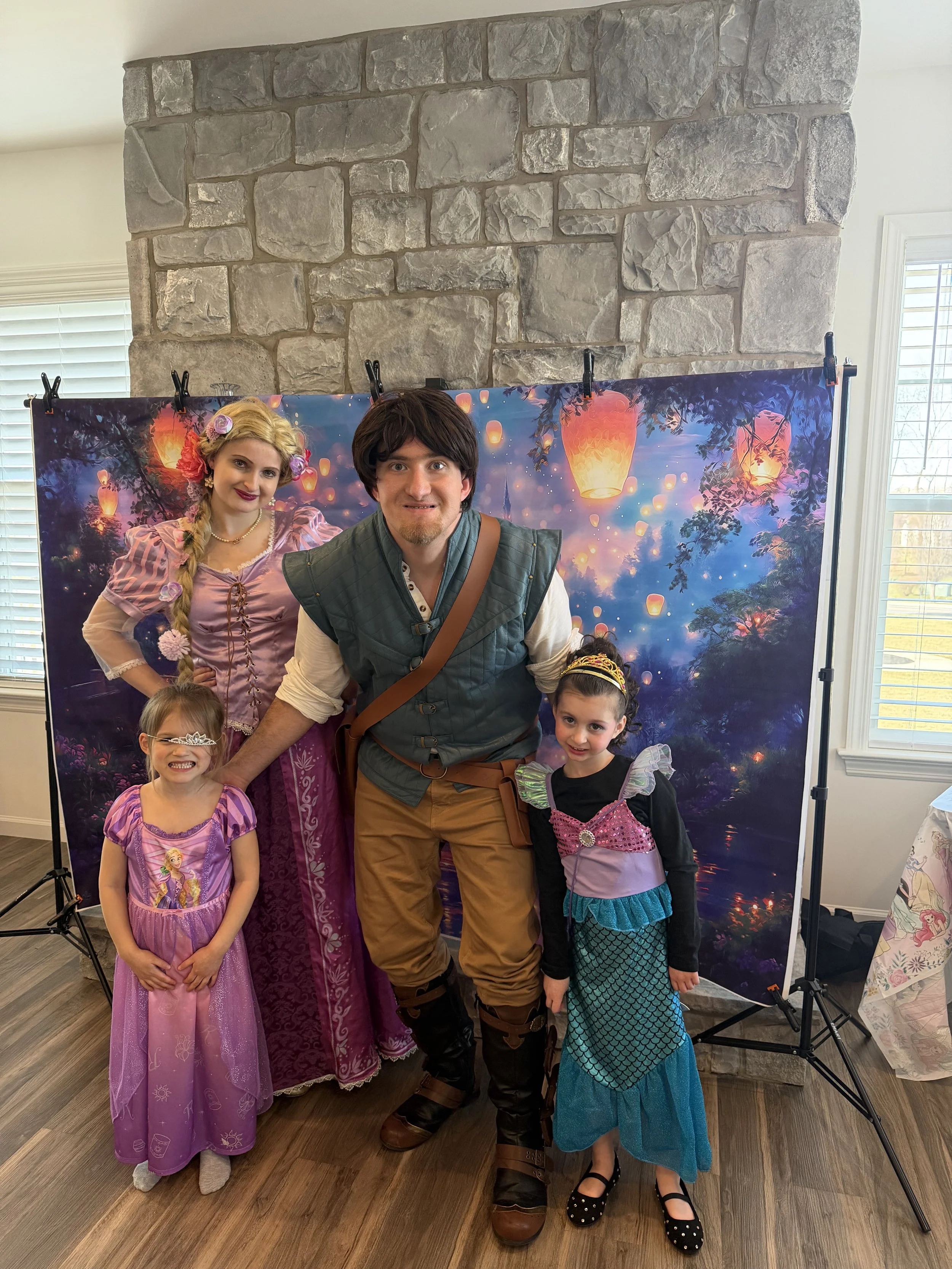 People dressed as characters from Tangled, Rapunzel and Flynn Rider, at a cosplay event with a fantasy sky backdrop showing lanterns.