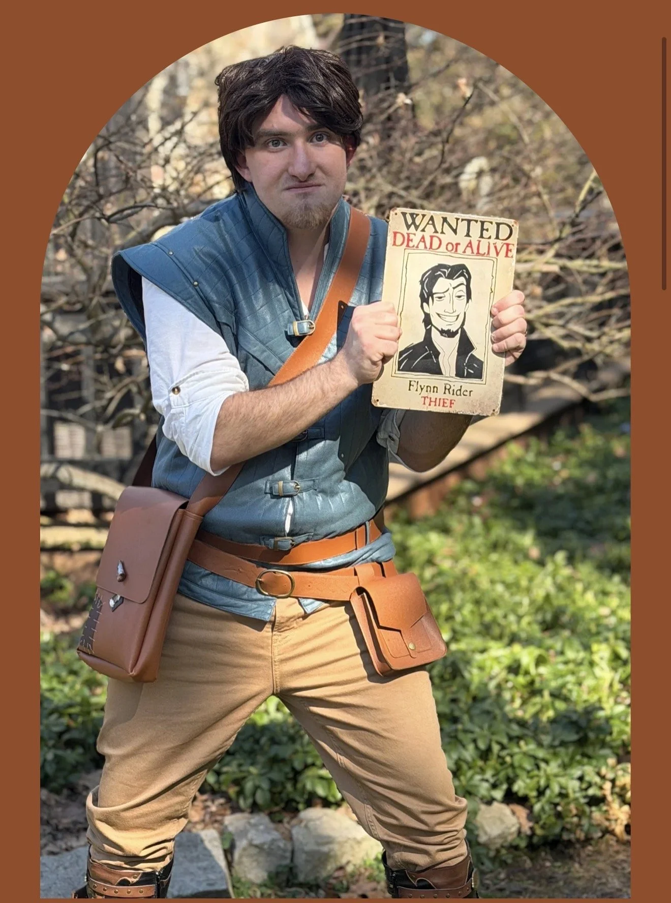 A person dressed as a fantasy character holding a wanted poster with a caricature of a man labeled as a thief named Flynn Rider.