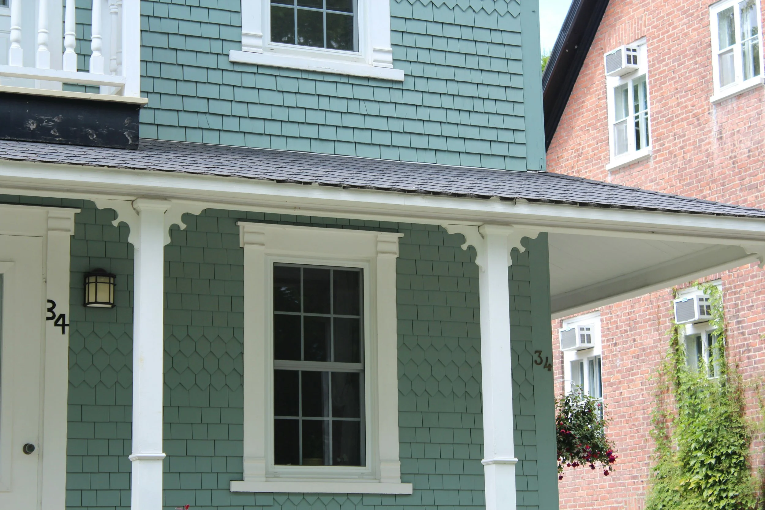 Close-up of a house's porch with a green painted exterior, white trim, a window, and a hanging flower basket.