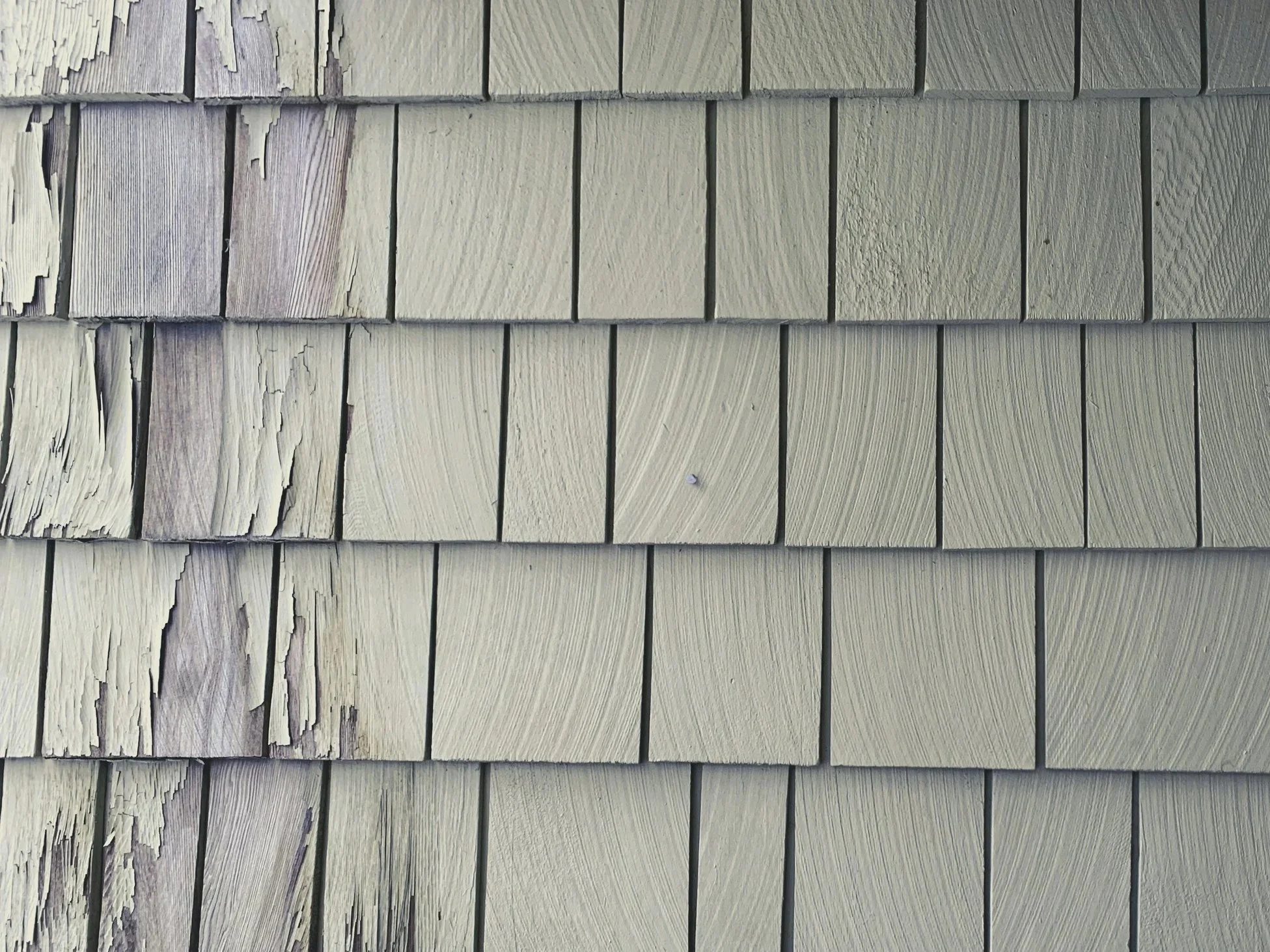 Close-up of a wooden exterior wall with painted shingles, some peeling and weathered.