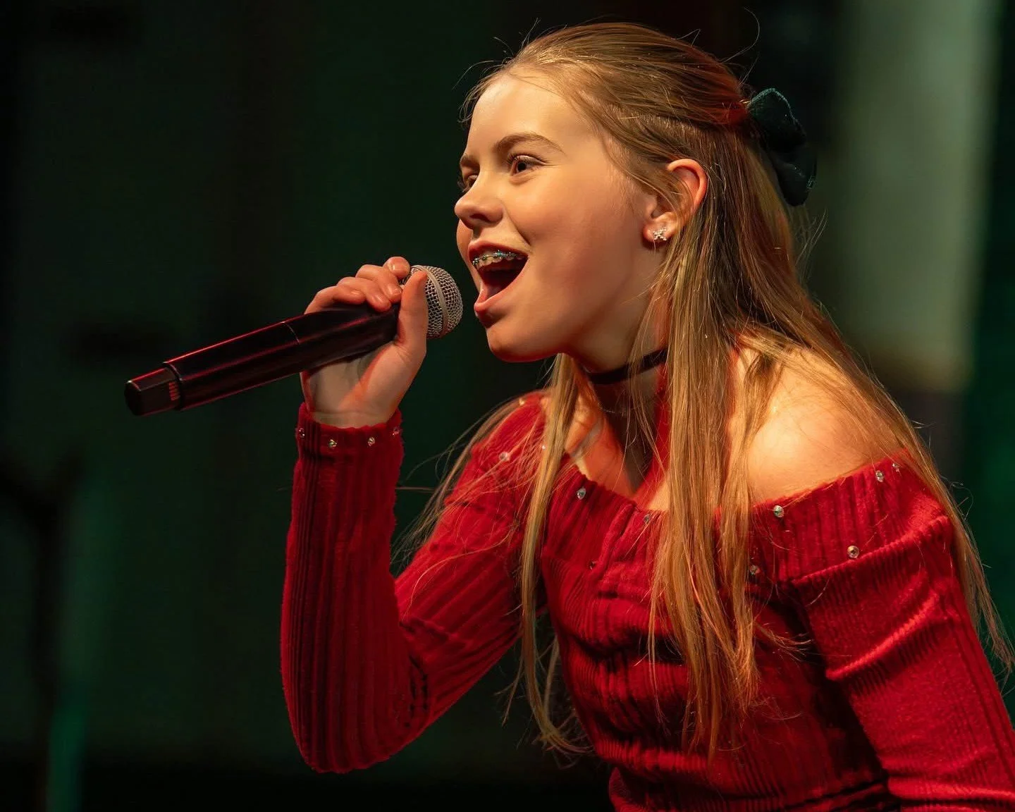 A blonde girl in a red dress singing into a microphone.