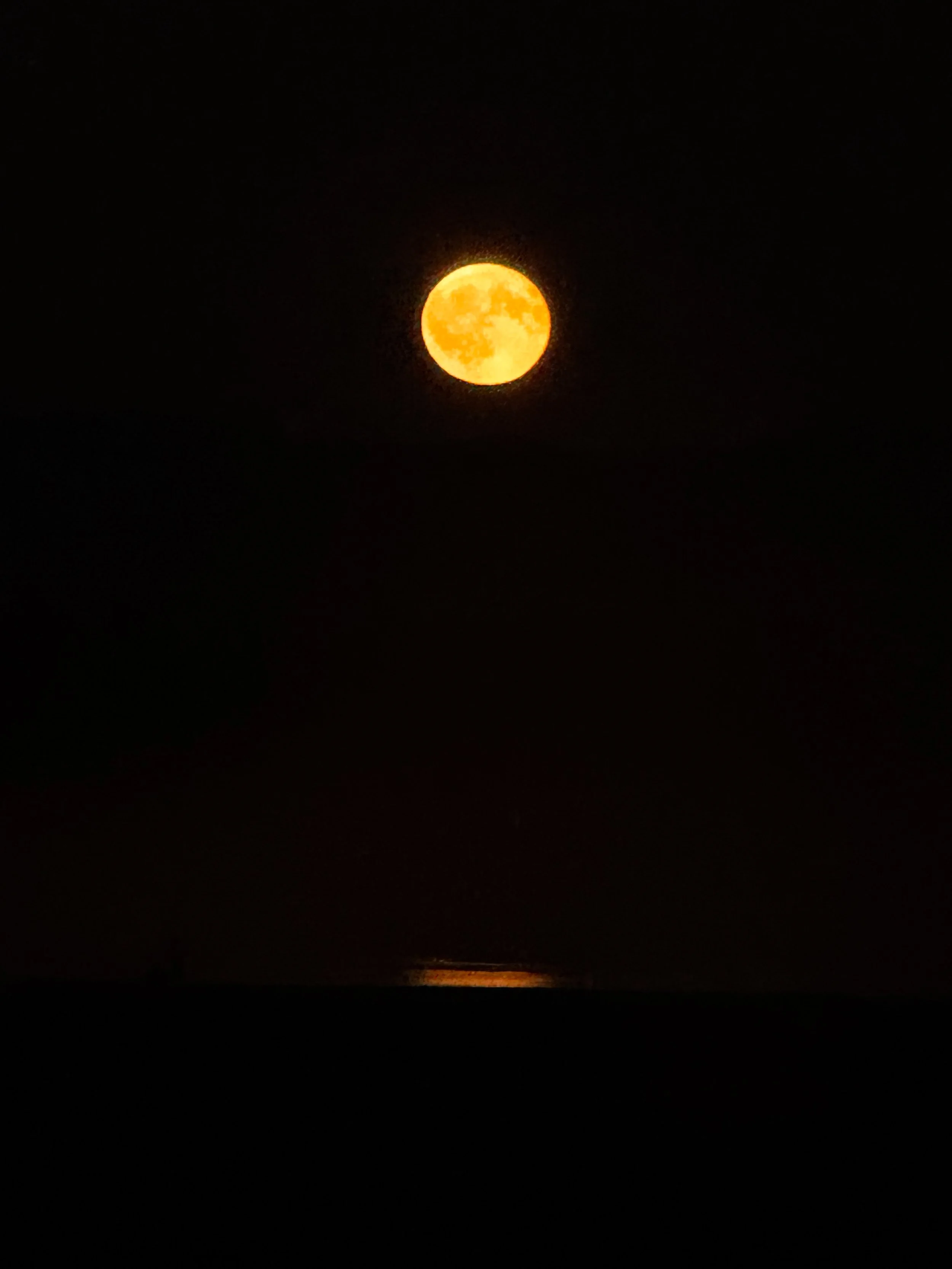 Full moon glowing yellow-orange in a dark night sky.