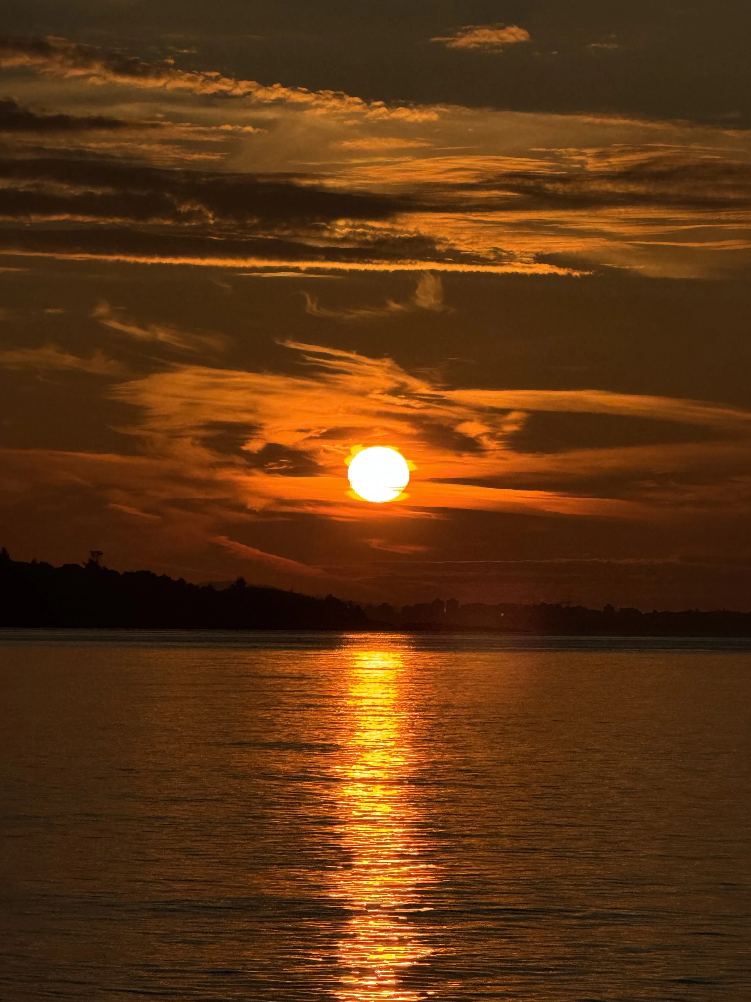 A sunset over a body of water with orange and yellow clouds in the sky, and the sun reflecting on the water.