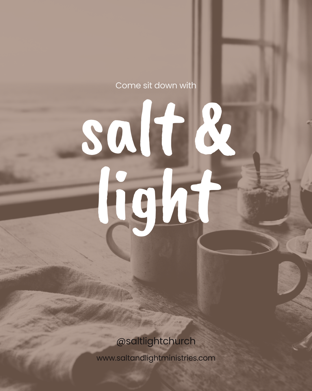 A cozy kitchen scene with two coffee mugs, a jar of salt, and a jar of sugar on a wooden table next to a window overlooking a beach. Overlaid text reads: "Come sit down with salt & light."