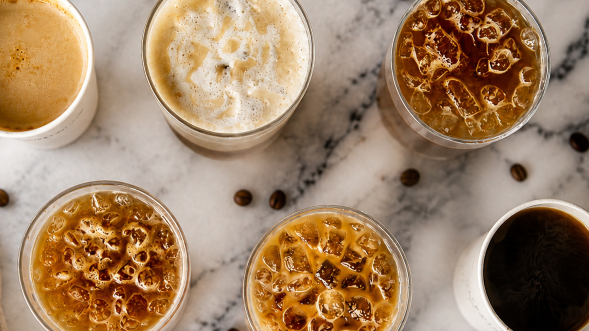 Multiple glasses of iced coffee with different colors and textures, placed on a white marble surface.
