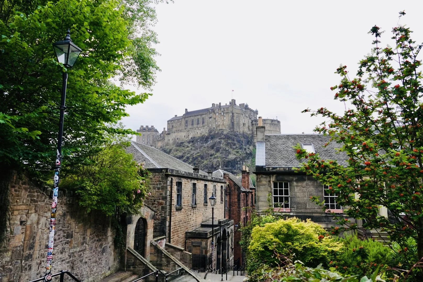 A castle on a hilltop surrounded by buildings, trees, and a cloudy sky in the background.