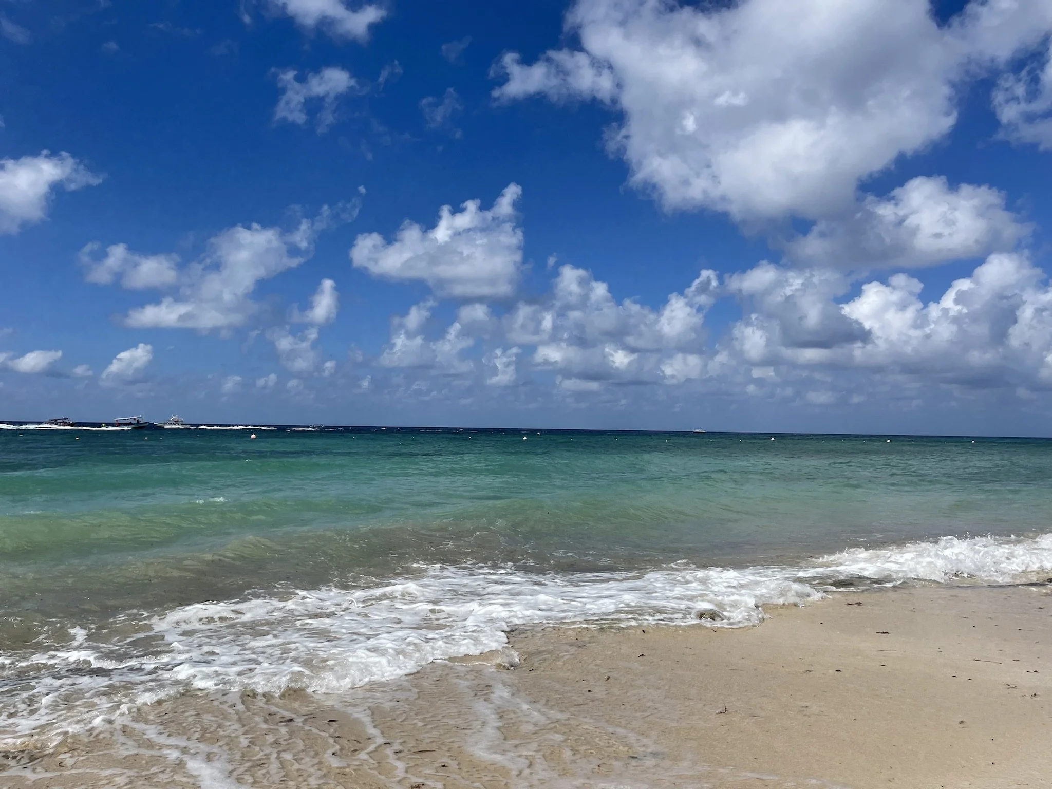 A sandy beach with gentle waves, turquoise water, and a partly cloudy blue sky.