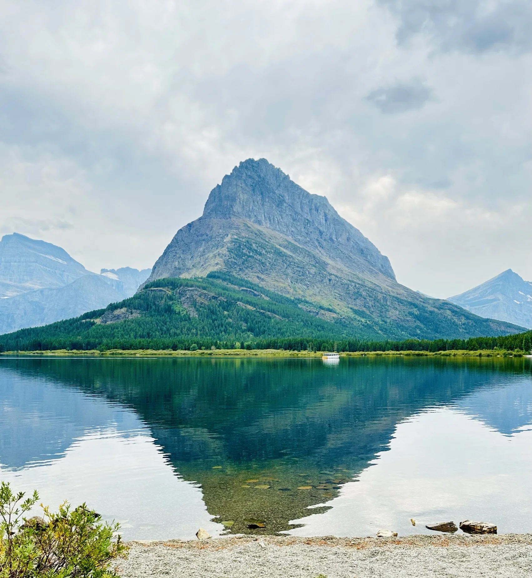 A mountain reflected in a calm lake with a cloudy sky overhead.