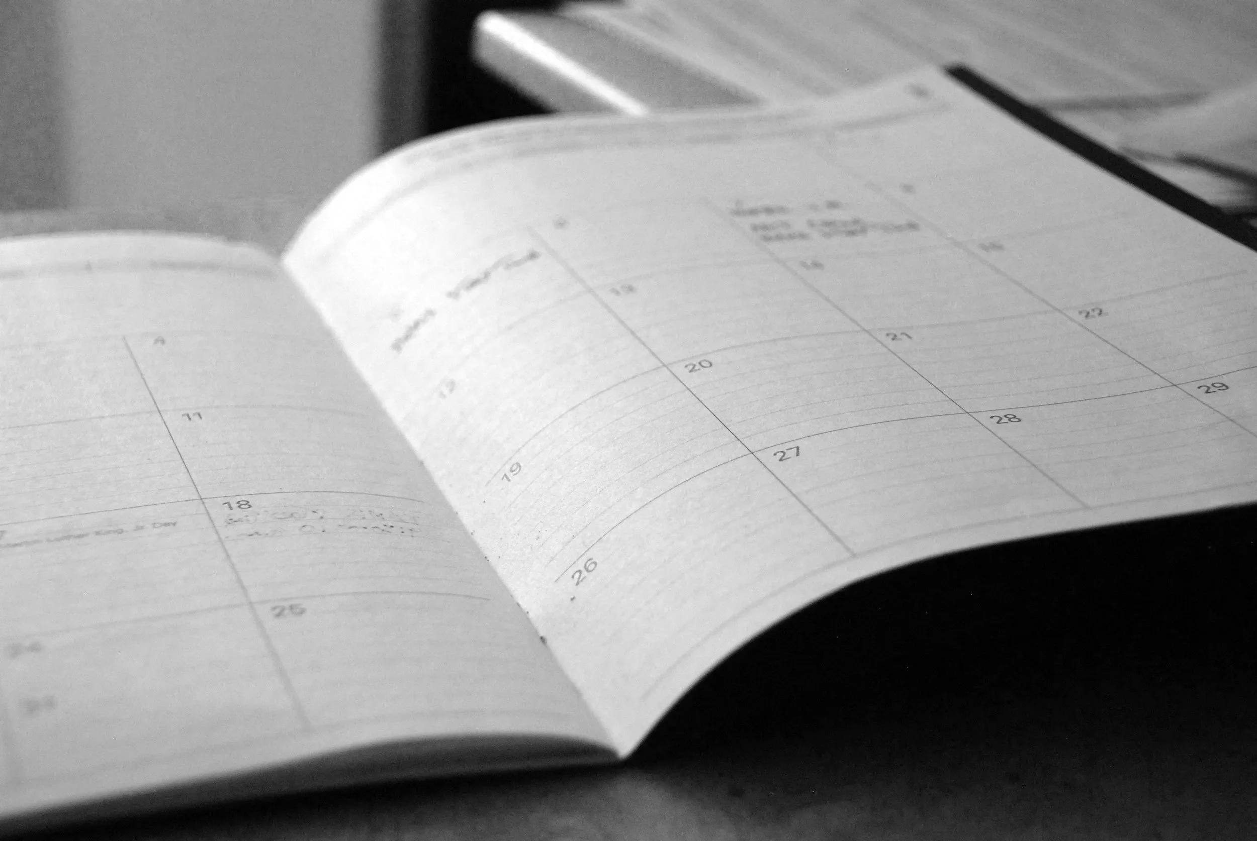 A black and white photo of an open planner or calendar on a desk, showing dates and appointments.