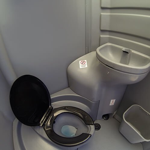 A compact bathroom with a toilet that has a built-in sink on top of the tank, and a small white trash bin beside it.