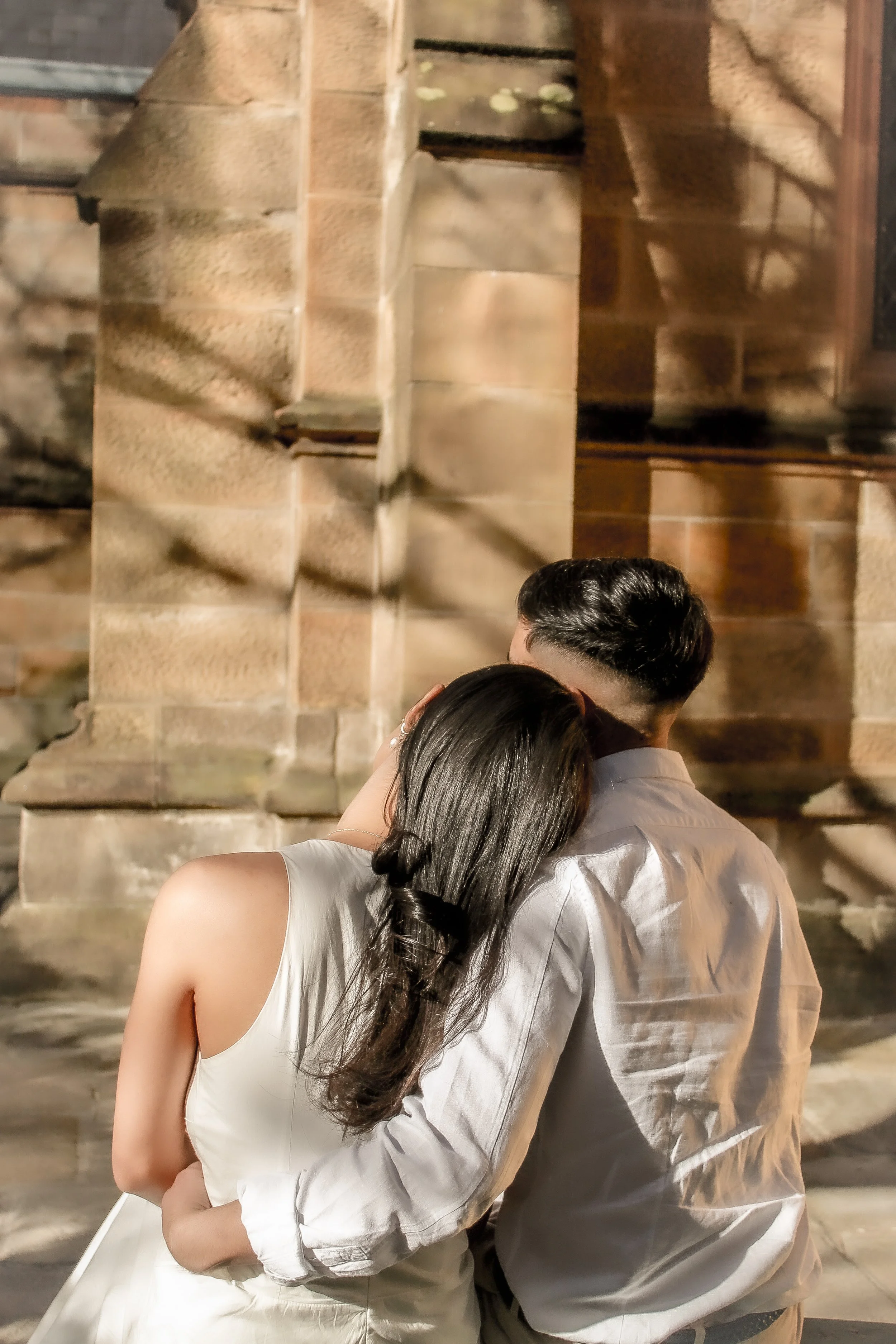 A couple hugging at night in front of a stone building with warm lighting.