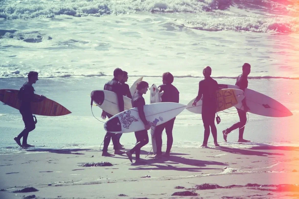 Group of young people carrying surfboards on the beach near the ocean.