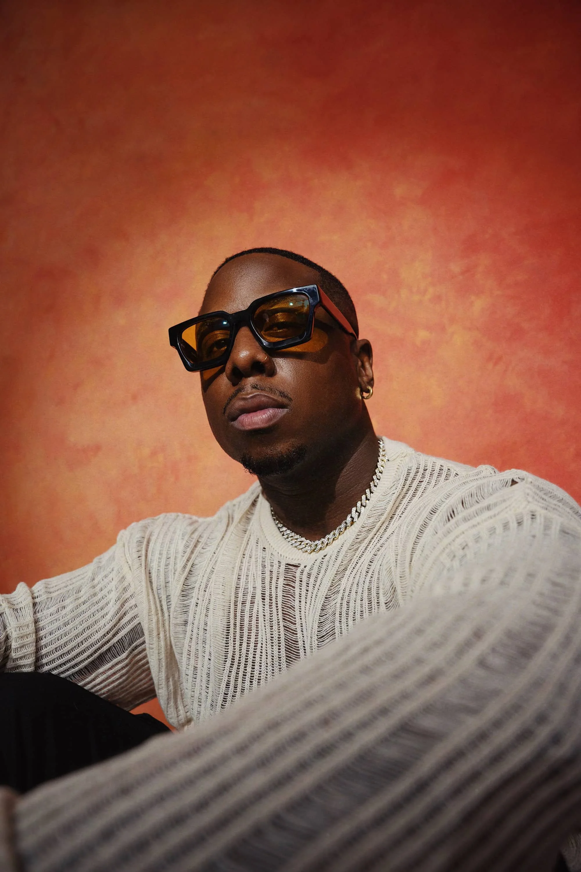 Aaron Hines, Fort Worth based R&B singer and soul artist, portrait with sunglasses and chain against an orange textured backdrop