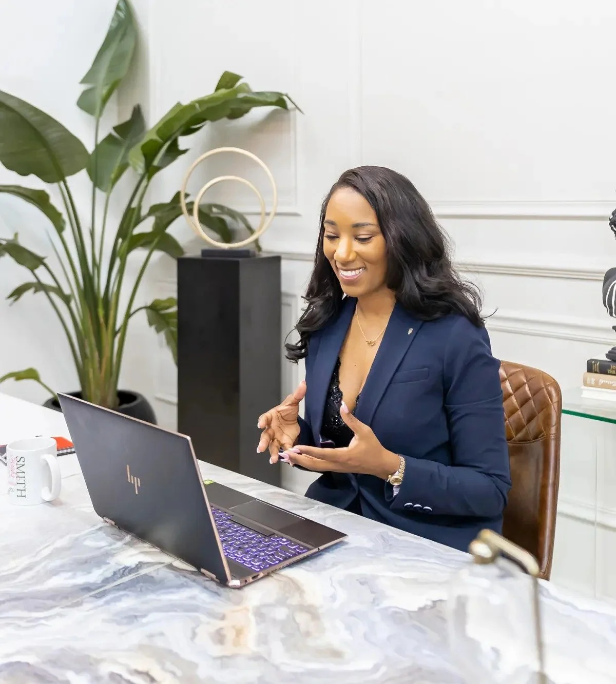Businesswoman sitting at a marble table, talking on her cellphone, with a laptop open in front of her, in a modern office setting.