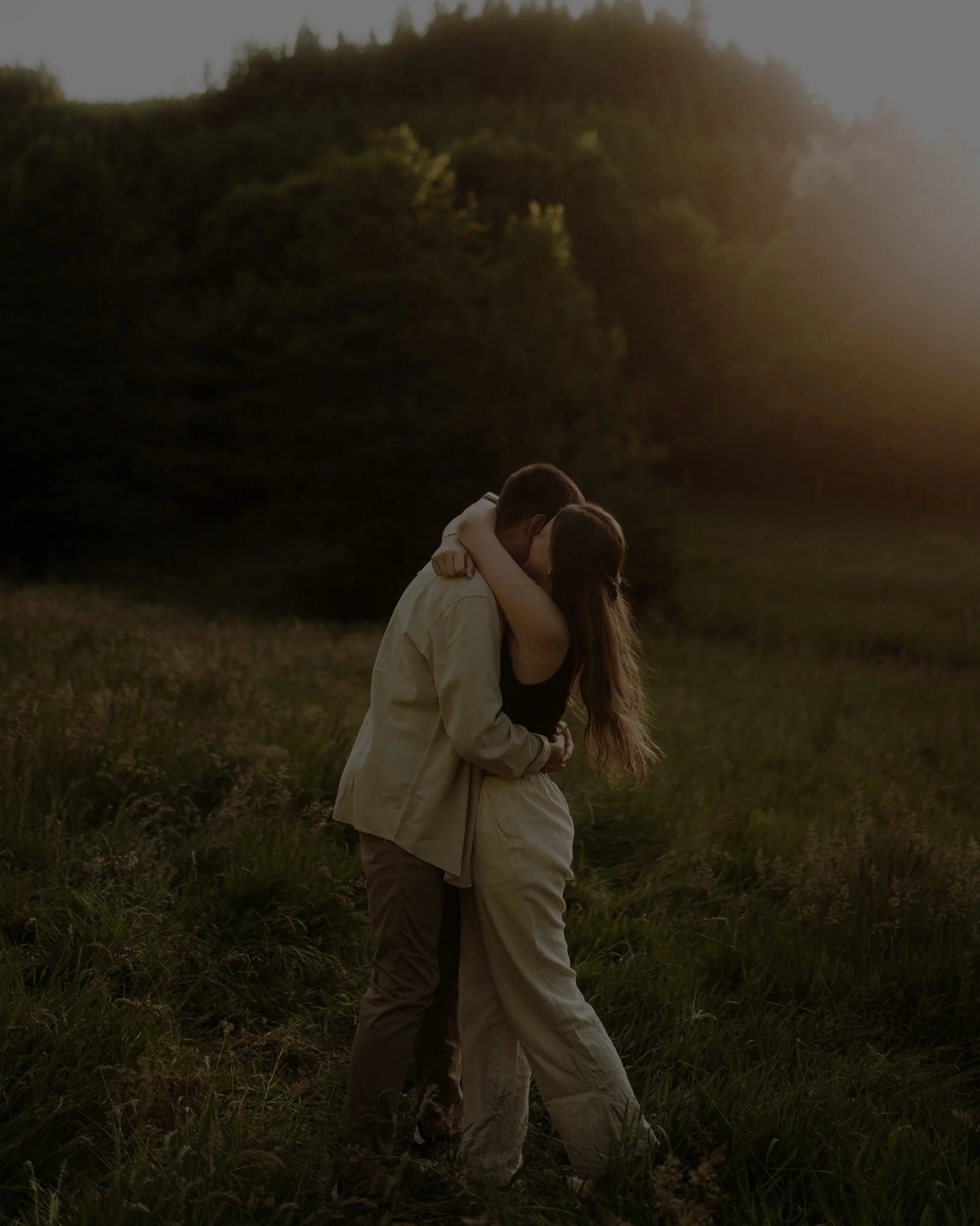 Ein Paar umarmt sich in einer Wiese bei Sonnenuntergang.