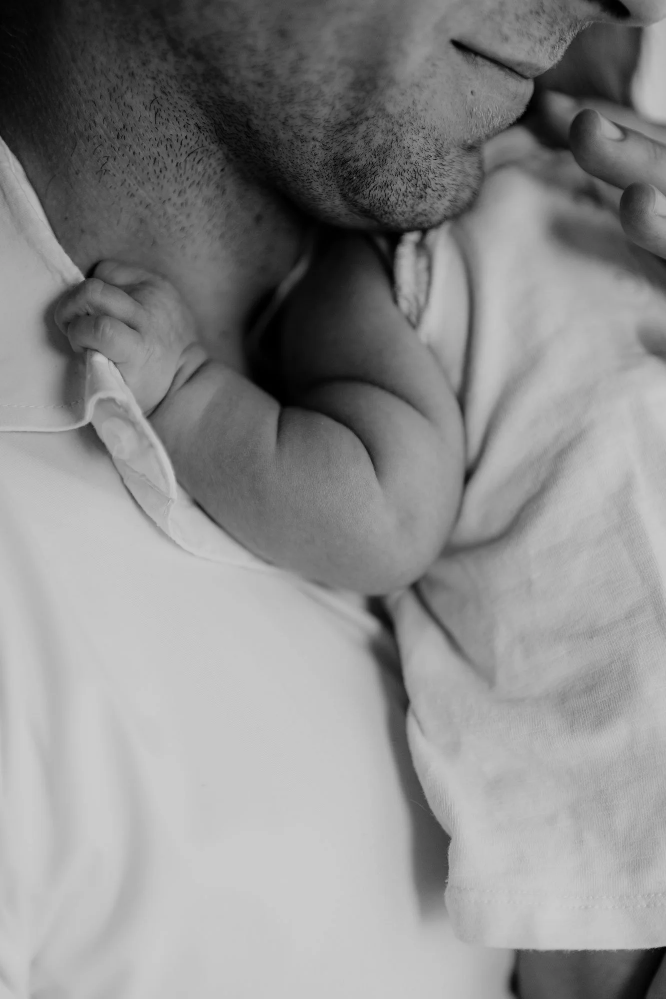 Nahaufnahme eines Mannes, der ein Baby hält, das mit seinem Arm um seinen Hals liegt. Das Bild ist schwarz-weiß und zeigt nur den Mund des Mannes, den Hals des Babys und die Hand des Babys, das den Hals umklammert.