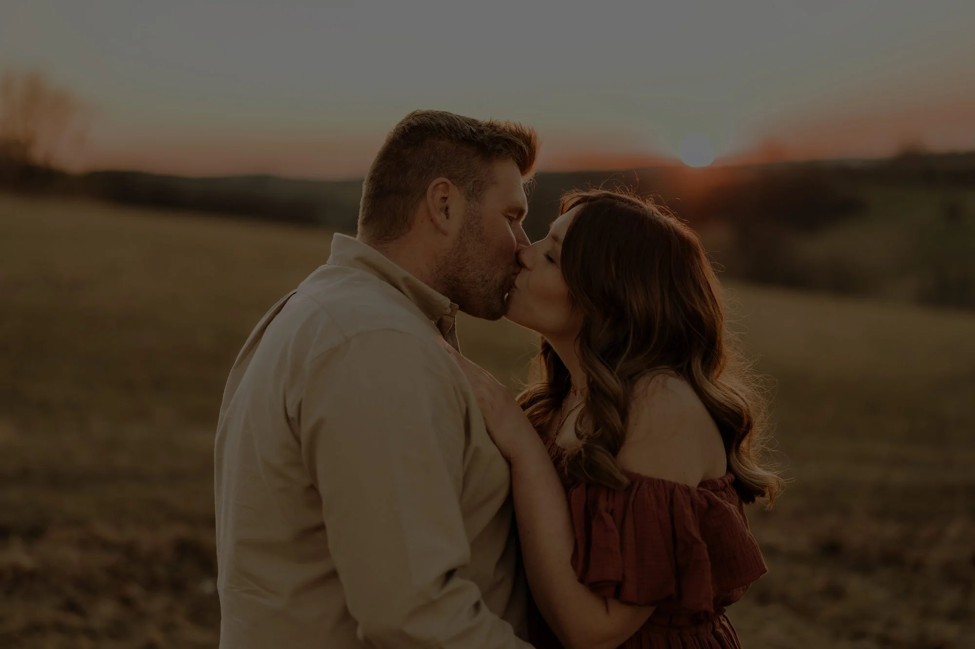 Paar küsst sich bei Sonnenuntergang auf einer ländlichen Wiese.