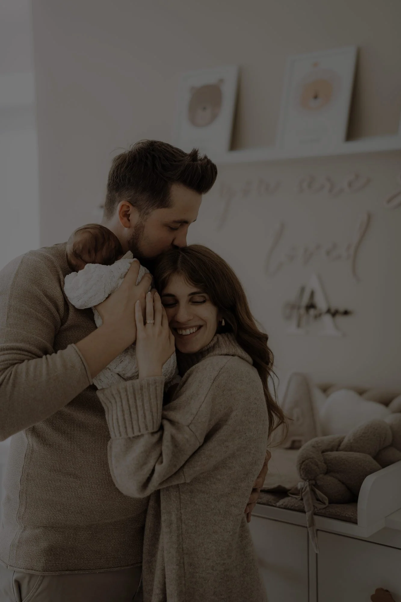 Ein glückliches Paar hält ein Baby in einem Raum mit dekorativen Wandbildern und Aufbewahrungsboxen, die Szene strahlt Liebe und Freude aus.