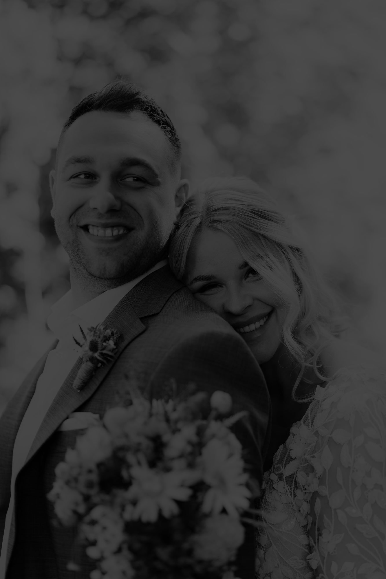 Schwarz-Weiß-Foto eines glücklichen Paares an ihrem Hochzeitstag, lachend und nah beieinander, mit Blumen im Vordergrund.